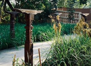 Zona exterior rústica amb una estructura de fusta, possiblement un banc o un element decoratiu, envoltada de vegetació abundant i un camí.