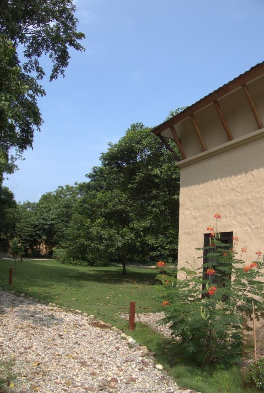 Un edificio de fachada color beige, un sendero de grava y una zona verde con árboles.