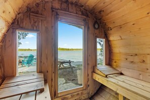 A cabin with a large window, wooden benches, and a view of a lake. - Redstart Retreat | Hot Tub | Sauna | Waterfront | EV | (Miller Lake)