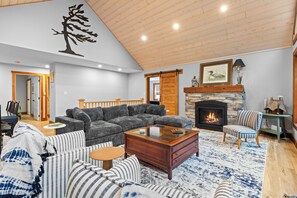A spacious living room with a large grey sectional sofa, a wooden coffee table, and a fireplace. - Redstart Retreat | Hot Tub | Sauna | Waterfront | EV | (Miller Lake)