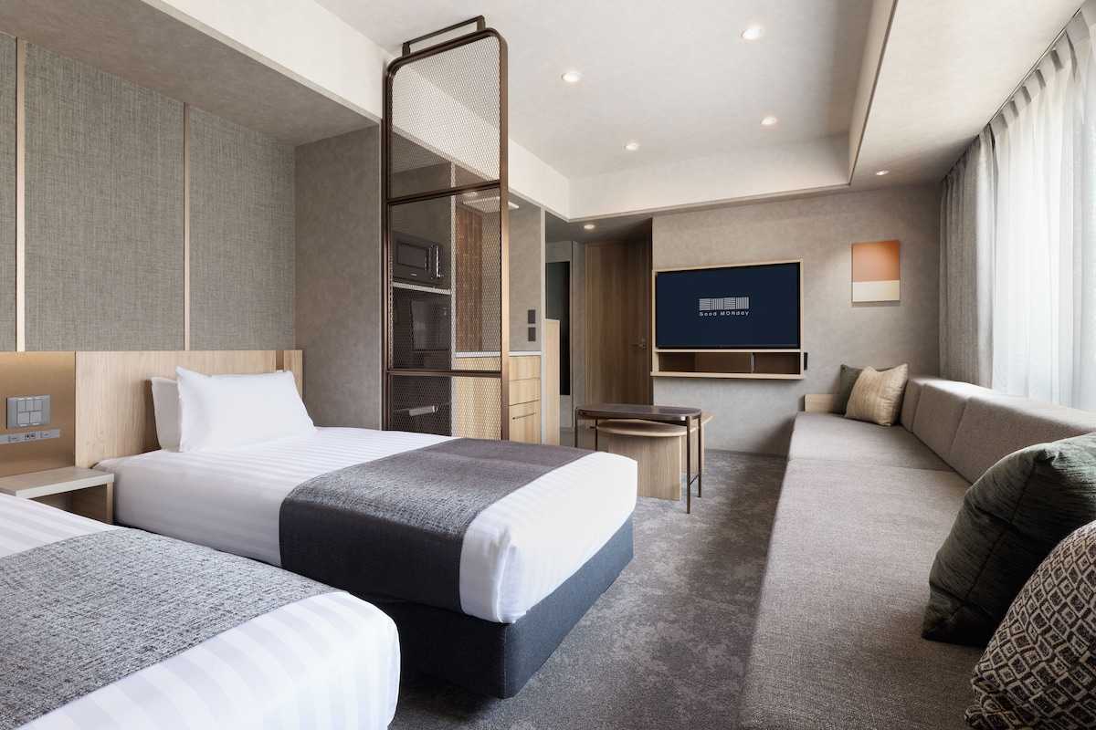 A hotel room with a bed, a seating area, a TV, and a wardrobe.