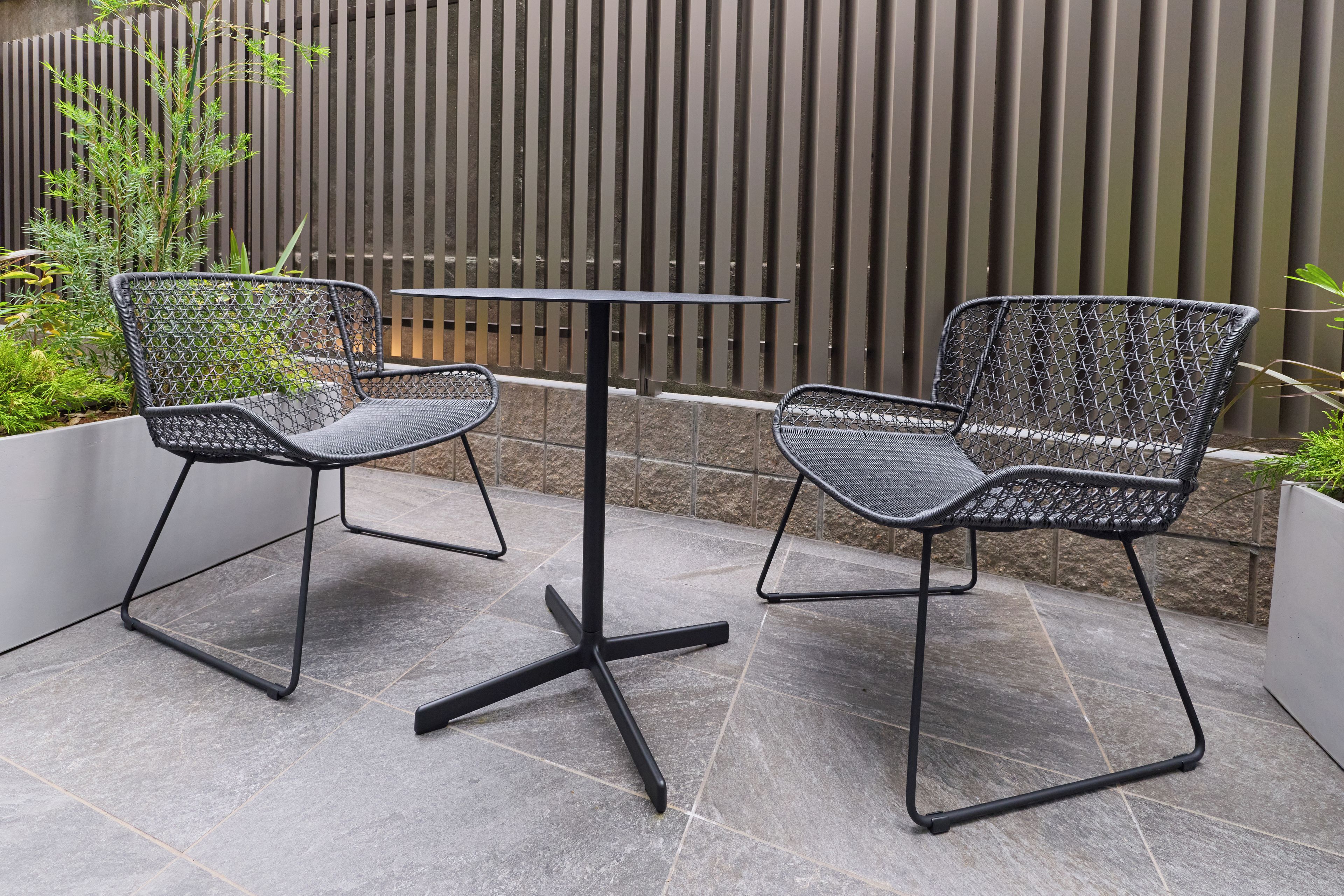 Two black wire mesh chairs and a small table with a black metal frame, placed on a tiled patio area.