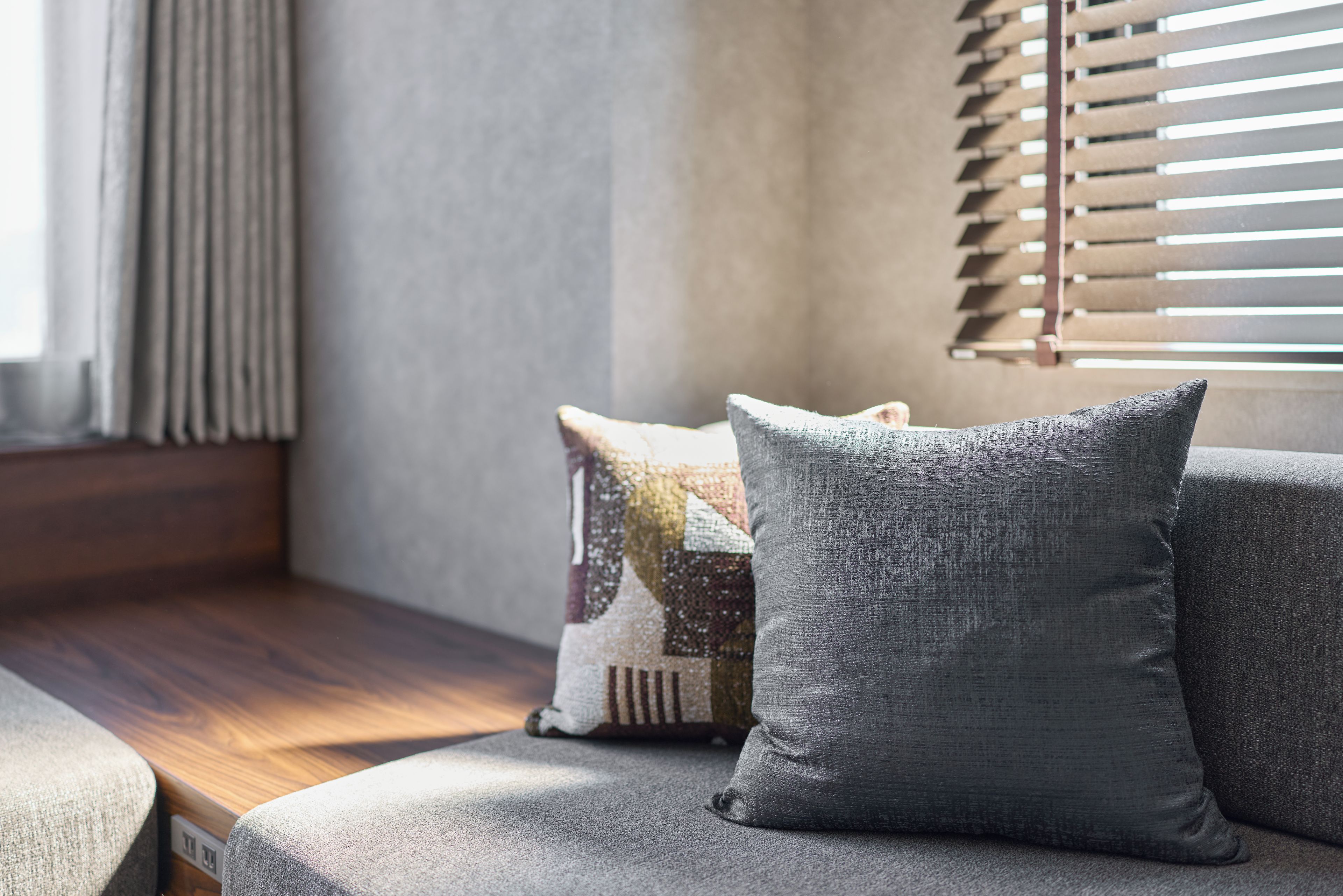 A corner of a room with a cushioned bench, a window with blinds, and a wall with a textured finish.