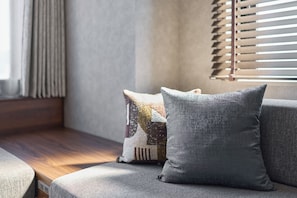 A corner of a room with a cushioned bench, a window with blinds, and a wall with a textured finish. - Good MONday ASAKUSA (Tokyo)