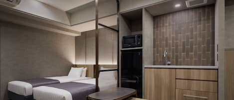 Habitación de hotel moderna con dos camas, una mesita, kitchenette y armario.