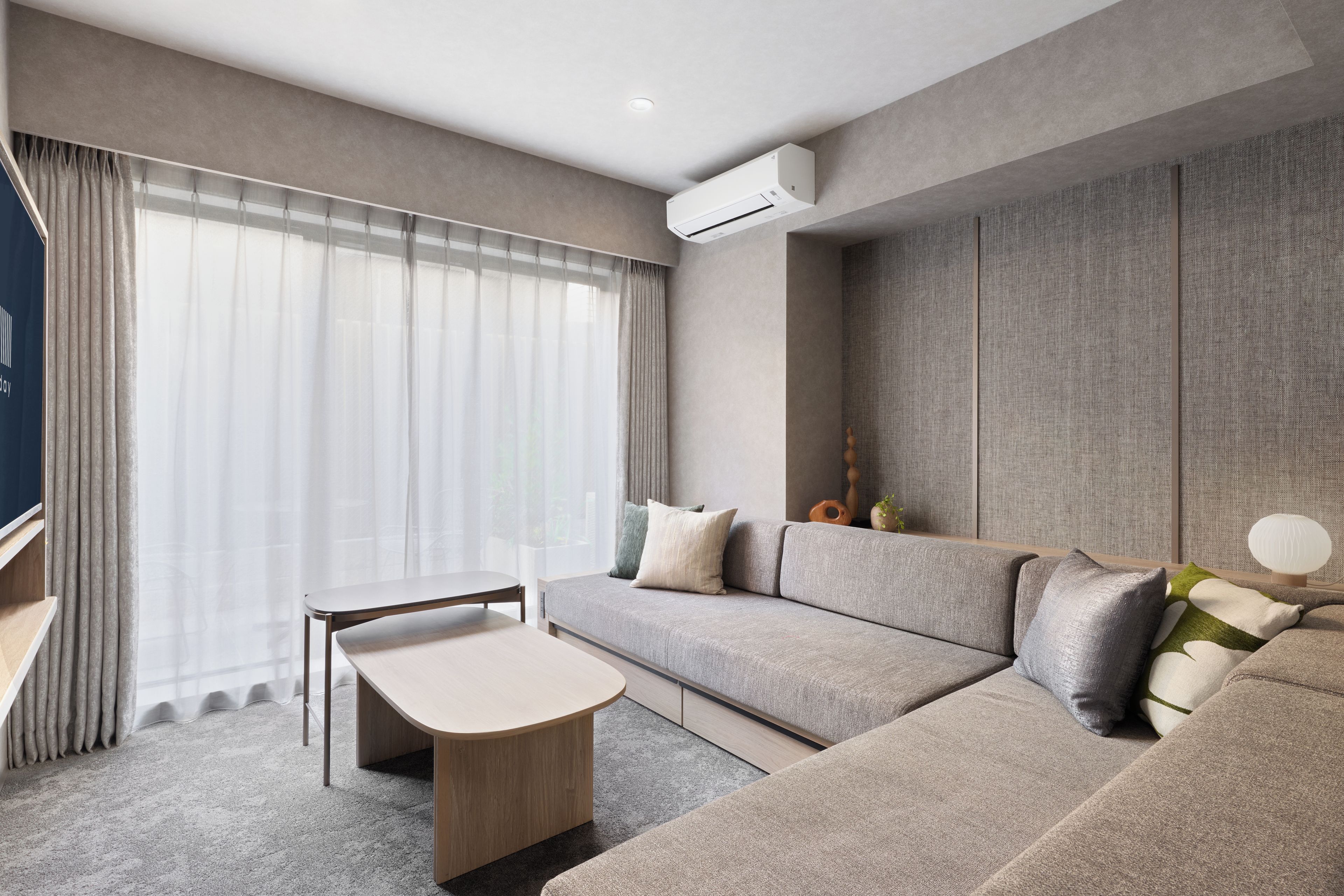 Una sala moderna con sof á modular, una mesita y un amplio ventanal con cortinas traslúcidas.