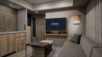 A modern living room with a flat-screen TV mounted on the wall, a sofa, a small table, and a kitchen area with wooden cabinets and a sink.