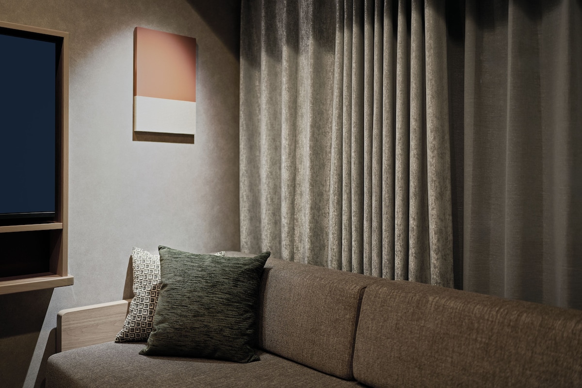 A modern living room with a sofa, a television, and a window with curtains.