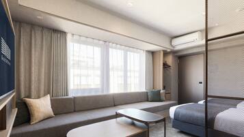 A modern hotel room with a sofa, a small table, a bed, and a large window with curtains.