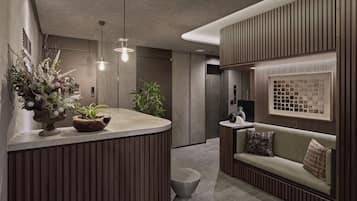 A modern reception area with a wooden reception desk, a seating area with a sofa and cushions, and a large potted plant.
