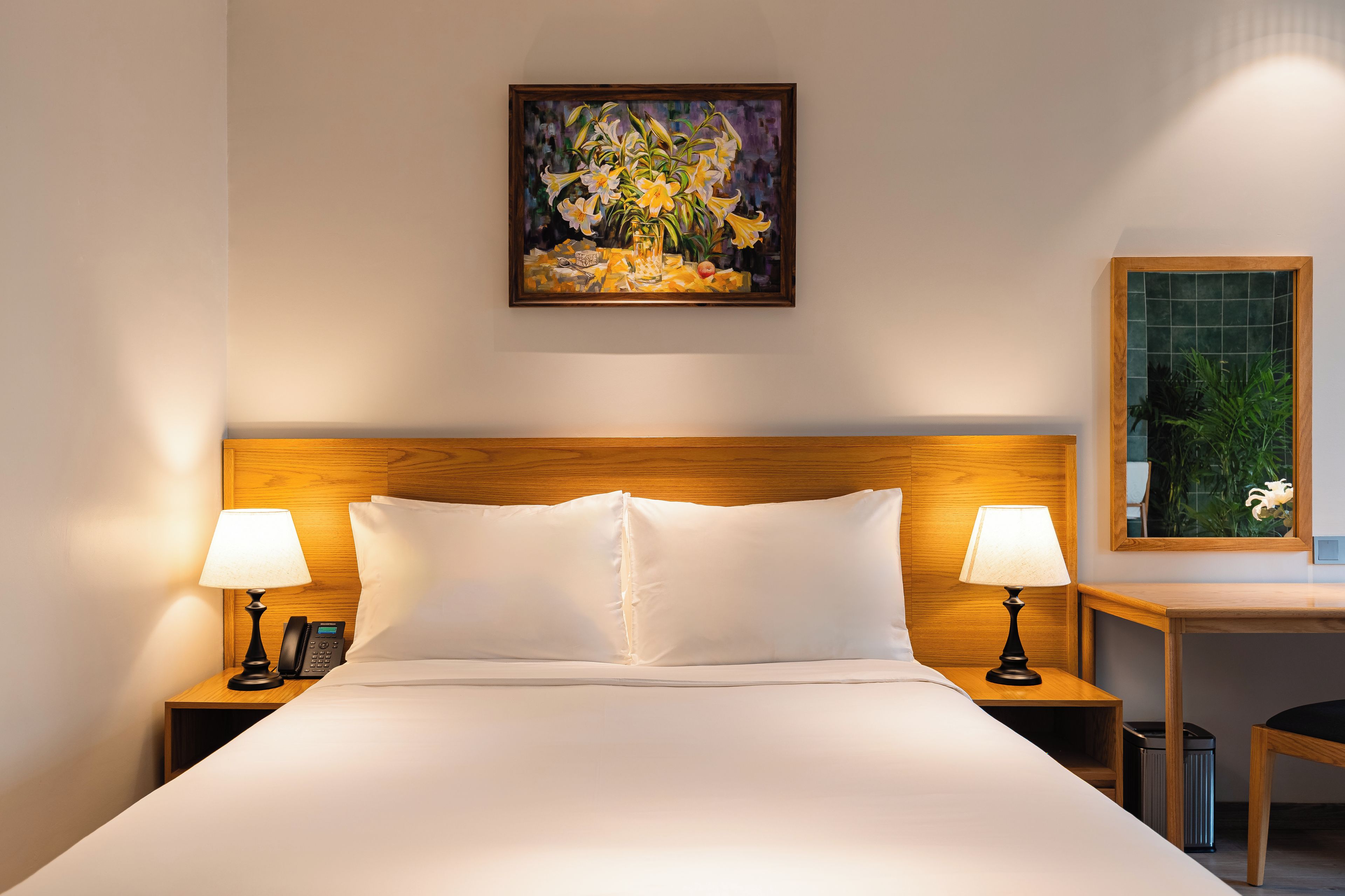 Habitación de hotel con cama, dos lámparas de noche, un teléfono, un cuadro en la pared y una mesita con una planta.