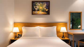 Habitación de hotel con cama, dos lámparas de noche, un teléfono, un cuadro en la pared y una mesita con una planta.