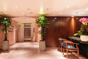 A hotel lobby with a reception desk, wooden paneling, potted plants, and an elevator.