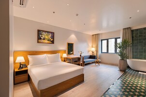 A hotel room with a large bed, a desk, a chair, a sofa, a bathroom with a bathtub, and a large window.