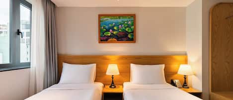 A hotel room with two beds, a painting of water lilies on the wall, and a view of buildings through the window.