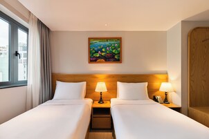 A hotel room with two beds, a painting of water lilies on the wall, and a view of buildings through the window.