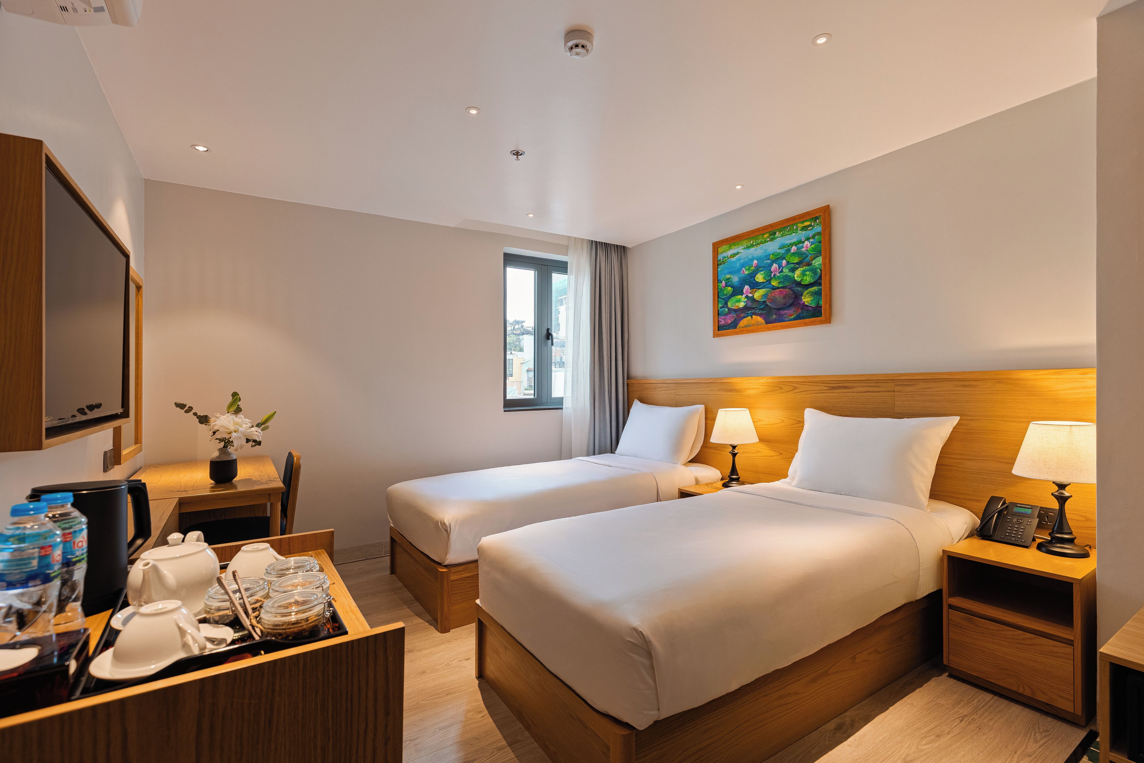 Ein Hotelzimmer mit zwei Betten, einem Schreibtisch mit Kaffeemaschine, einem Telefon und einem Bild an der Wand.