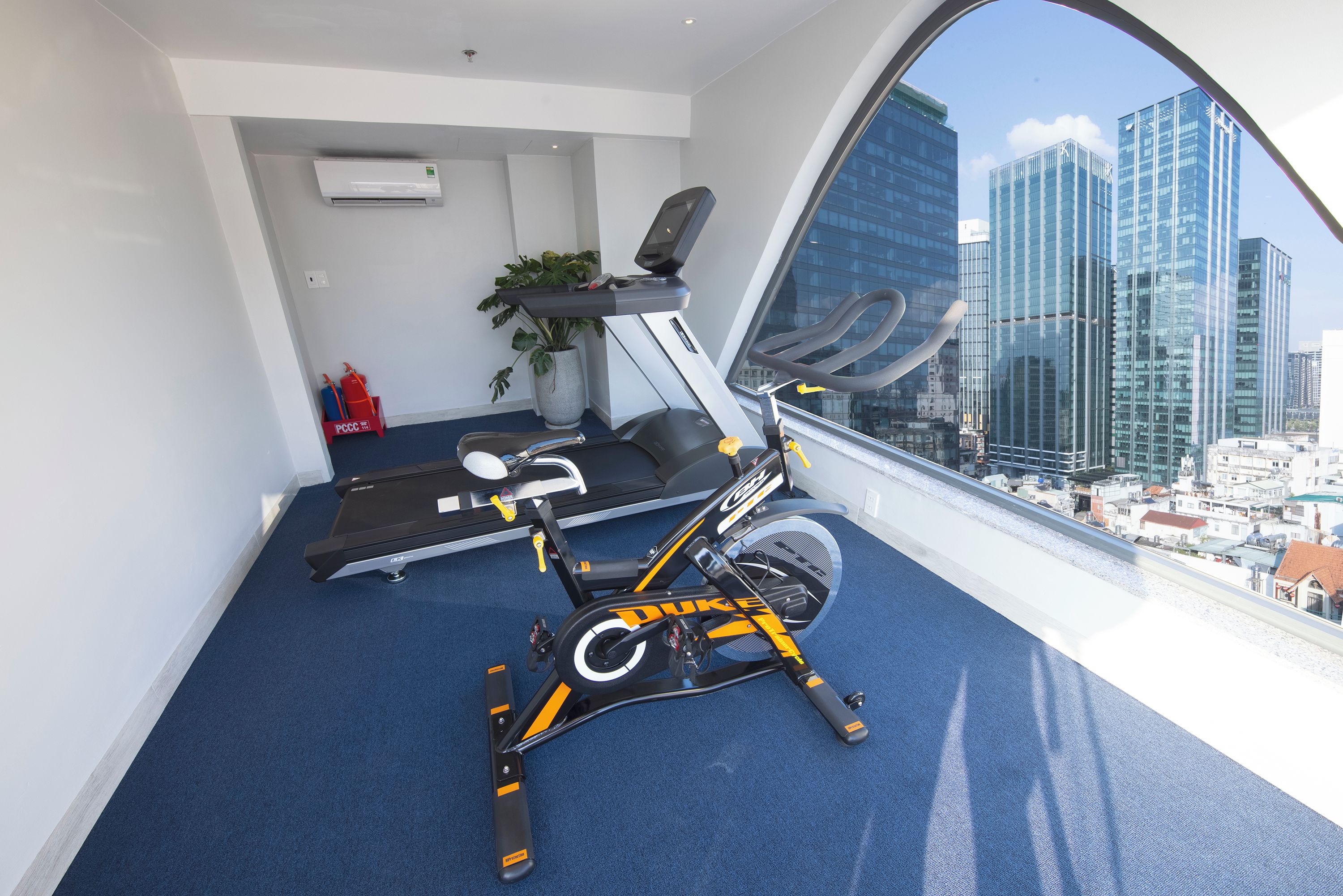 Un gimnasio con equipo de ejercicio y un amplio ventanal con vistas a un paisaje urbano.
