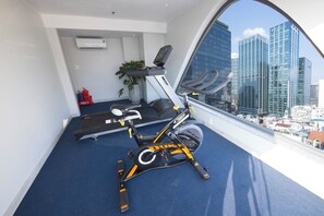 Une salle de sport équipée de matériel d’exercice et dotée d’une grande fenêtre donnant sur un panorama urbain.