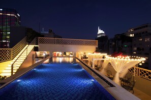 Une piscine sur le toit offrant une vue sur les gratte-ciel illuminés d’une ville la nuit.