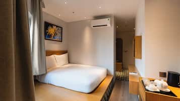 Una habitación de hotel con cama, un cuadro, unidad de aire acondicionado y una pequeña cocina.