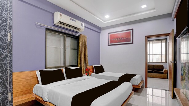 Habitación de hotel con dos camas, un equipo de aire acondicionado, una ventana con cortinas, un cuadro en la pared y una puerta que da a otra habitación.