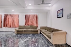A room with two sofas, a ceiling fan, and a painting on the wall. - Hotel O Saibaba Temple Formerly Sai (Rahata)