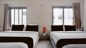 Habitación de hotel con dos camas, una mesita con un florero y una ventana con cortinas.