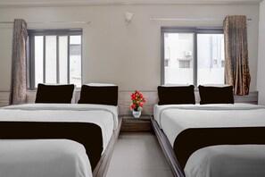 A hotel room with two beds, a small table with a vase of flowers, and a window with curtains. - Hotel O Saibaba Temple Formerly Sai (Rahata)