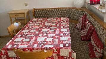 A dining area with a table covered in a red and white patterned tablecloth, a bench with red cushions, and a wall-mounted picture of a snowy landscape.