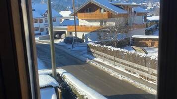 Blick aus dem Fenster auf eine Wohngegend mit Häusern, einer Straße und verschneiten Bergen im Hintergrund.