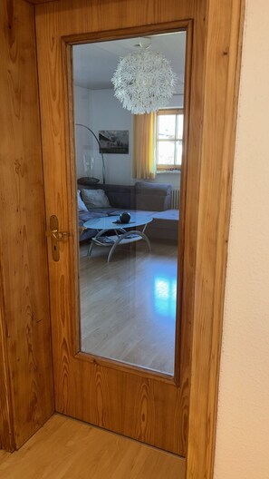 A wooden door with a glass panel reflecting a living room interior.