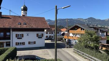 A residential area with a building featuring a clock tower, a street with parked cars, and a mountain backdrop.