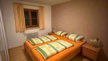 Ein Einzelzimmer mit einem hölzernen Bett, einem Nachttisch, einem Heizkörper und einem Fenster mit Vorhängen.