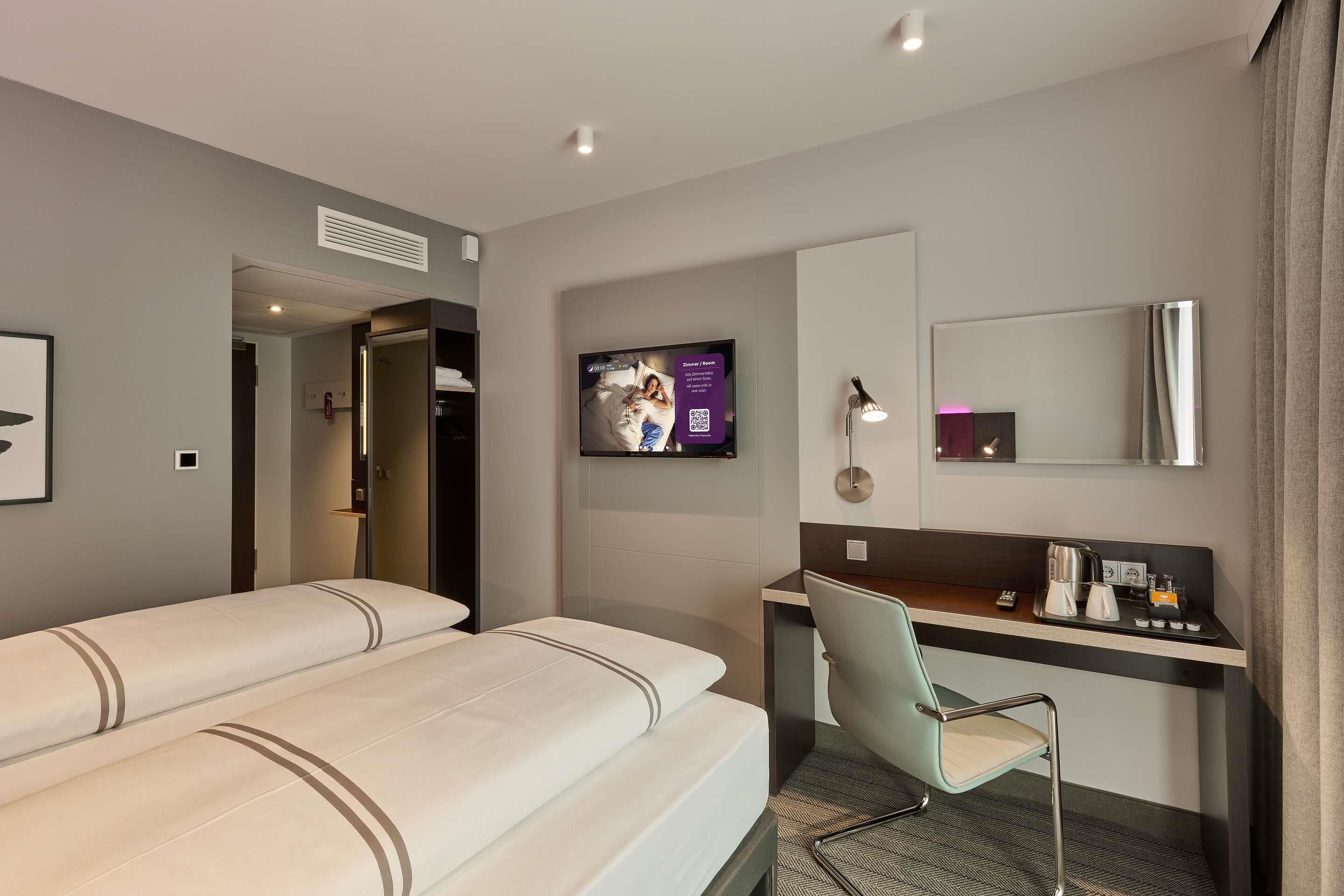 Una habitación de hotel con cama, escritorio, silla, televisor y espejo.