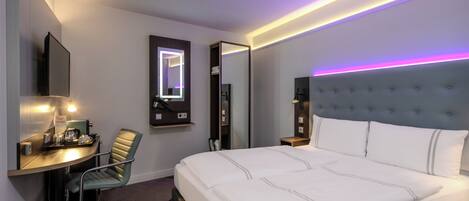 Une chambre d’hôtel équipée d’un lit, d’un bureau, d’une chaise, d’un miroir et d’un téléviseur fixé au mur.