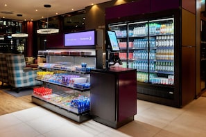 A hotel lobby with a self-service beverage station, a television screen, and seating area.