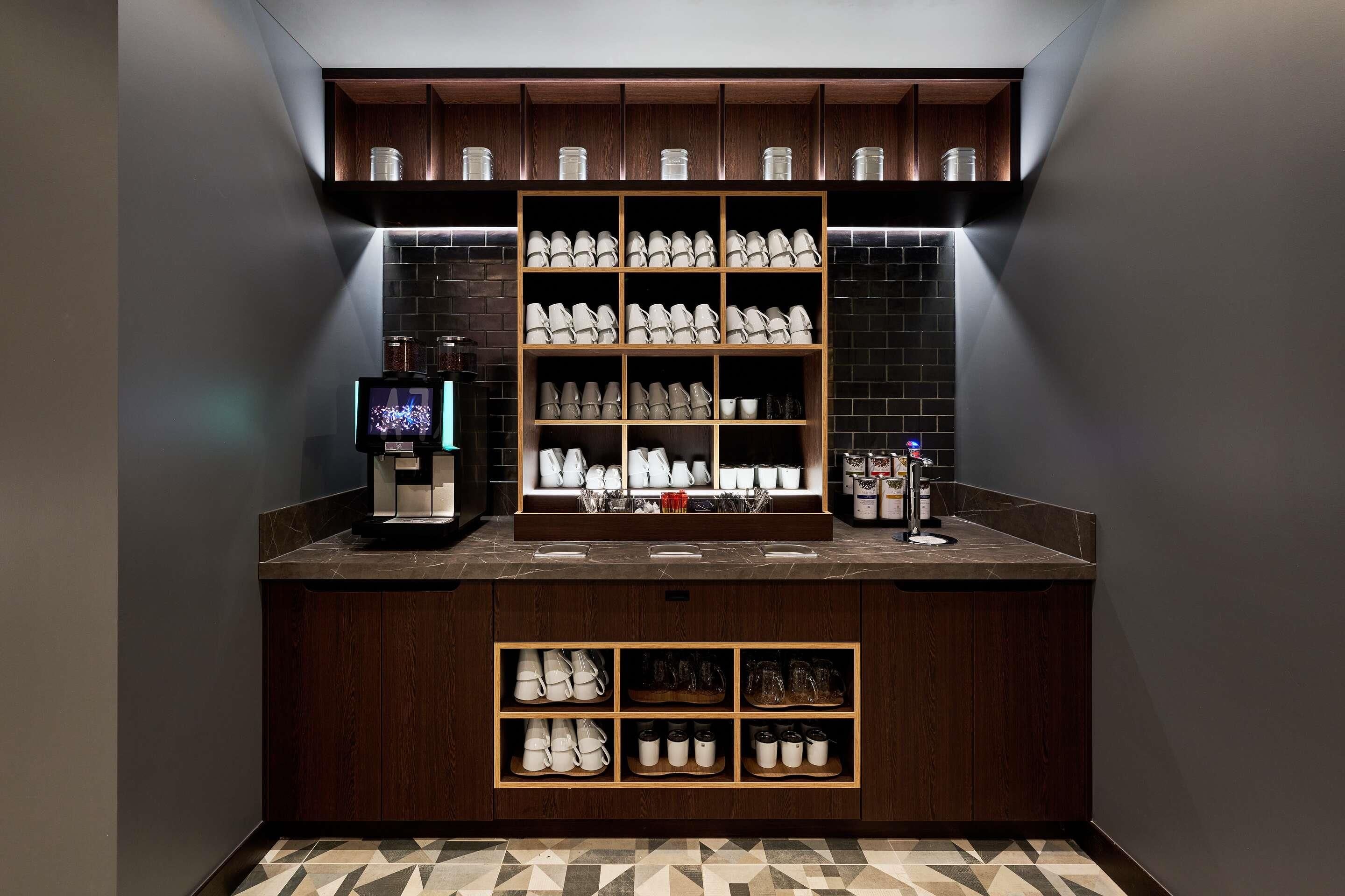 Une cuisine équipée d’une machine à café, d’étagères remplies de tasses et de bocaux, et d’un dosseret carrelé.