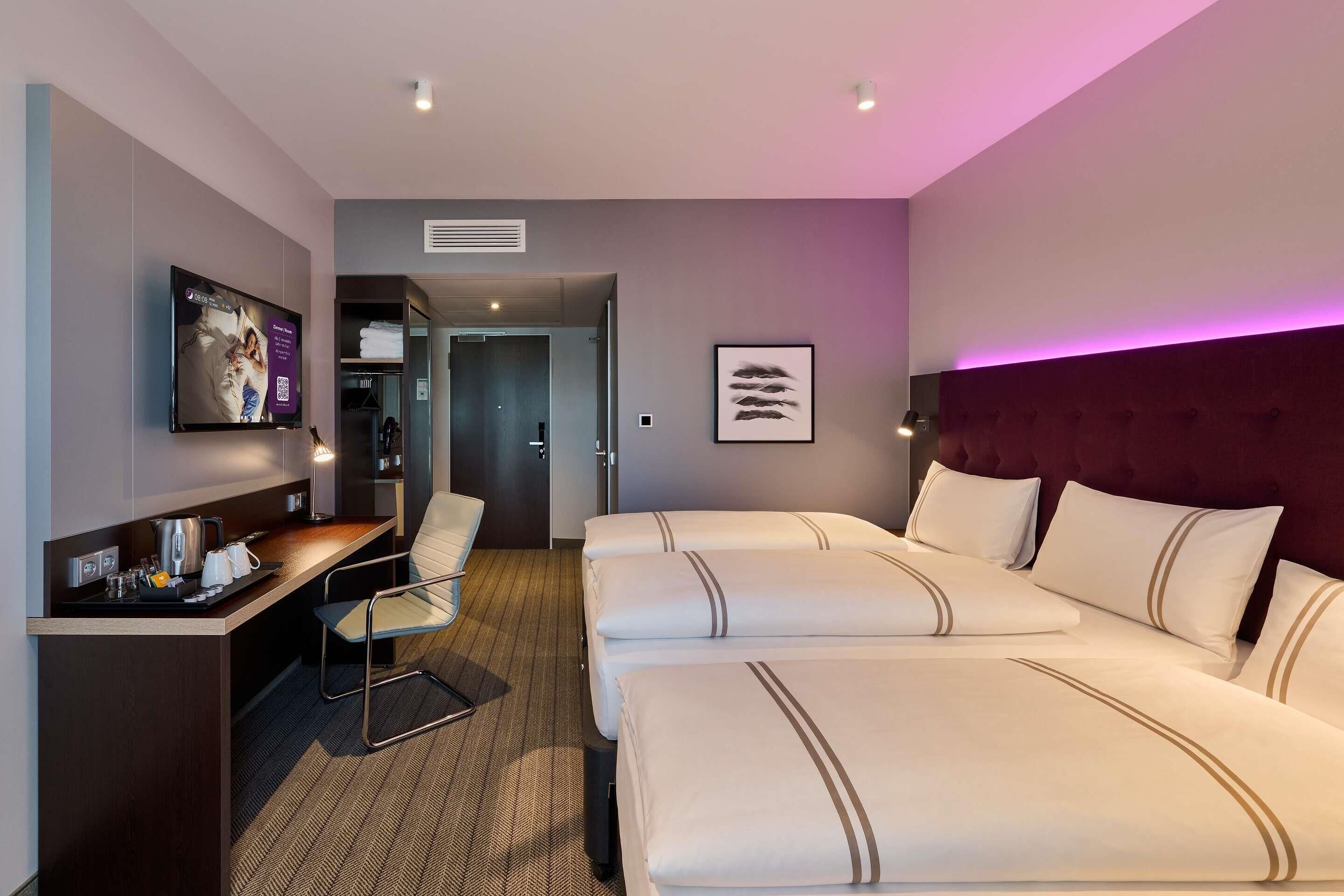Ein Hotelzimmer mit einem Bett, einem Schreibtisch, einem Stuhl, einer Kaffeemaschine und einem gerahmten Bild an der Wand.
