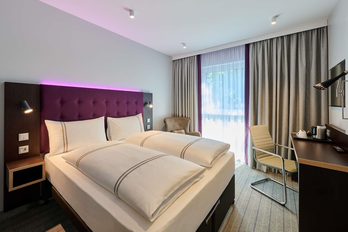 A hotel room with a large bed, a desk, a chair, and a view of the outdoors.
