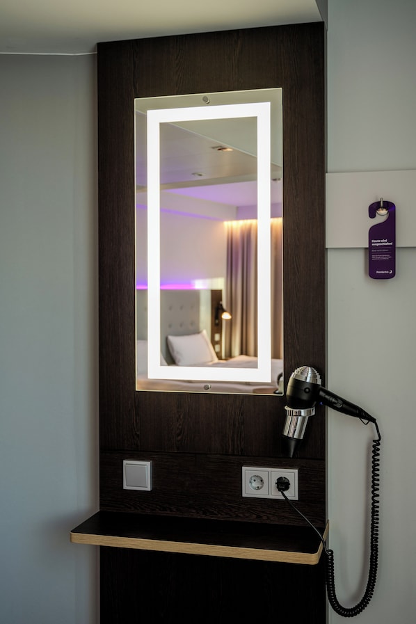 A hotel room with a mirror, a hairdryer, and a phone on a wooden counter. - Premier Inn Konstanz (Konstanz)