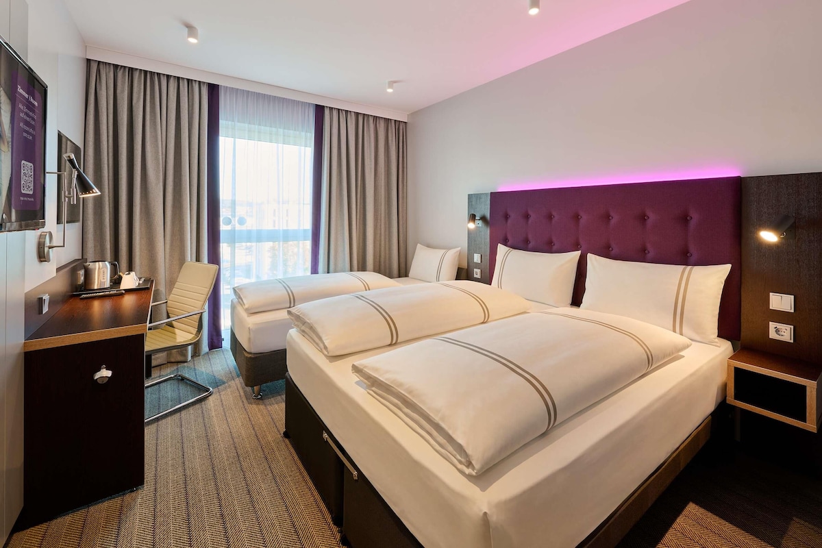 A hotel room with a large bed, a desk, a chair, and a view of the city.