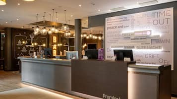Un espace d’accueil d’hôtel au design moderne, comprenant un comptoir d’accueil, un grand mur orné de textes et d’images, et de nombreux luminaires suspendus.