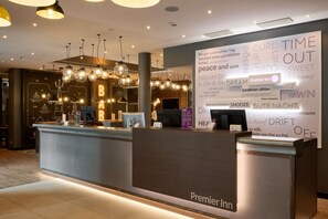 A hotel reception area with a modern design, featuring a reception desk, a large wall with text and images, and multiple hanging light fixtures.