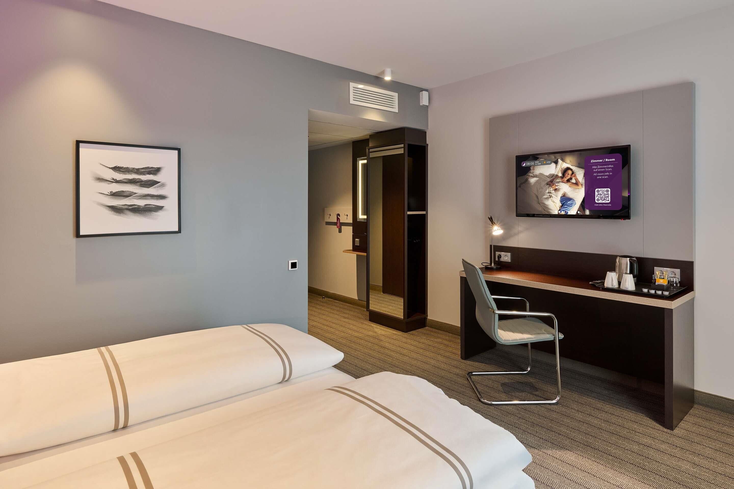 Ein Hotelzimmer mit zwei Betten, einem Schreibtisch mit Stuhl, einem Fernseher und einem gerahmten Bild an der Wand.