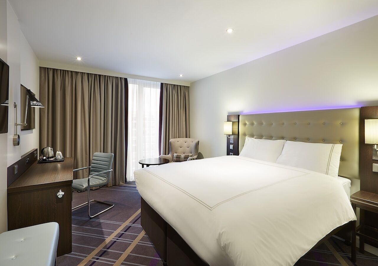 Ein Hotelzimmer mit einem großen Bett, einem Schreibtisch, einem Sessel, einem Nachttisch und einer Lampe.