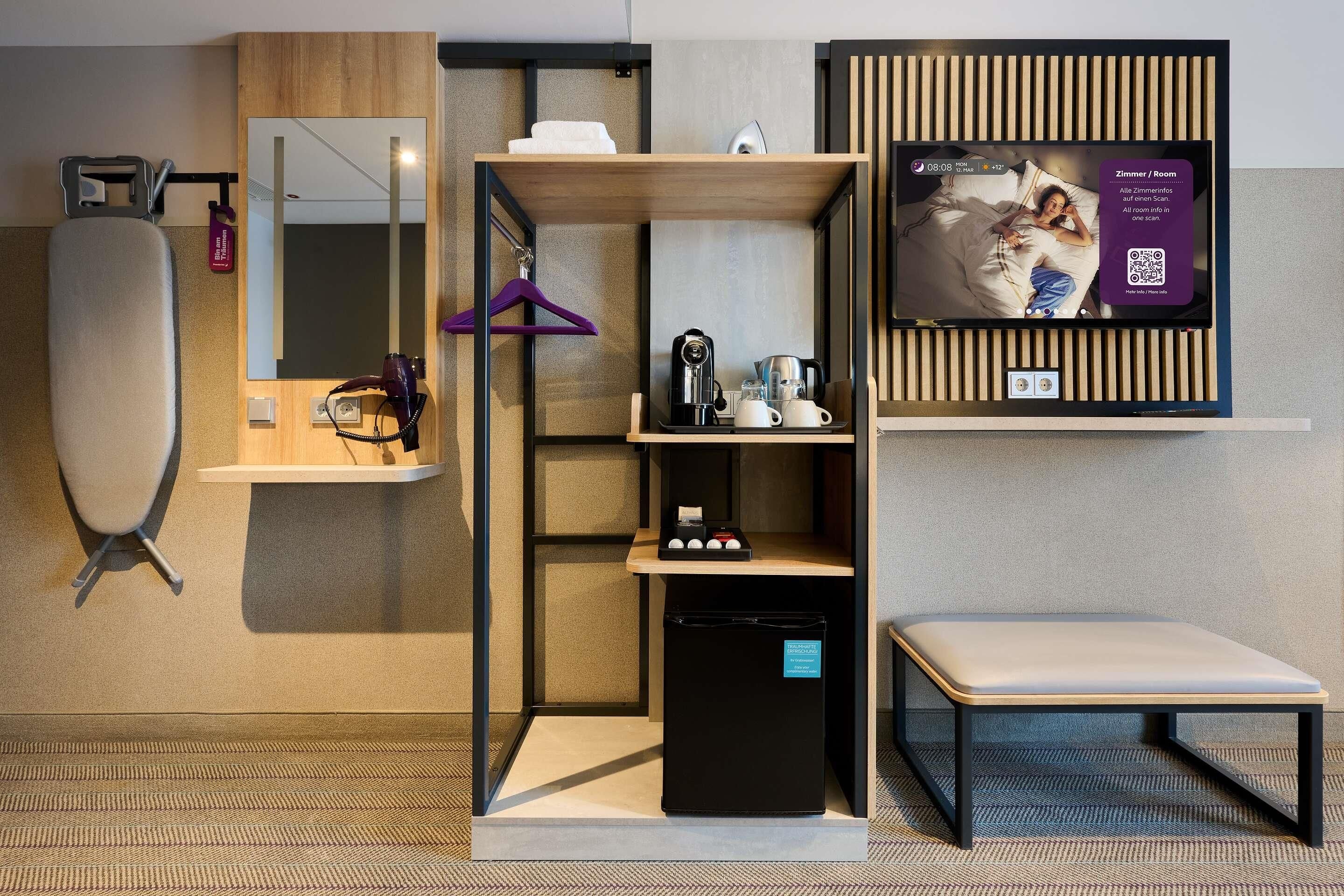 Ein modernes Hotelzimmer mit integriertem Fernseher, Fön, Spiegel und Ablage für Toilettenartikel.