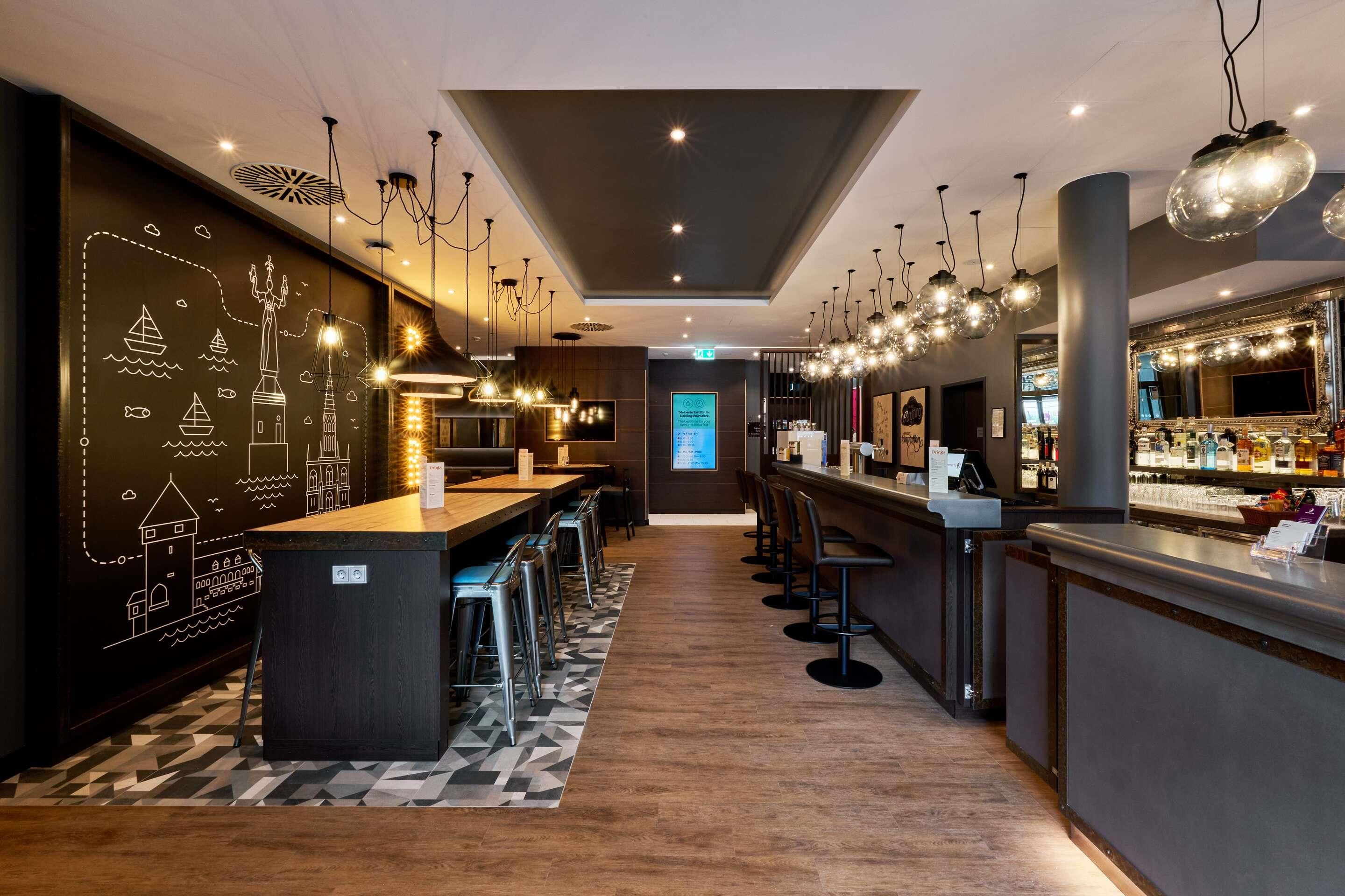 Zona de bar moderna con una barra larga, varios taburetes y una pared decorativa con ilustraciones náuticas.
