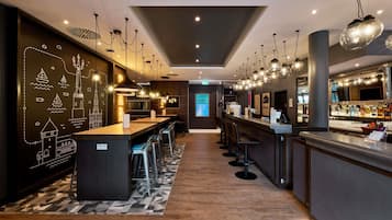Zona de bar moderna con una barra larga, varios taburetes y una pared decorativa con ilustraciones náuticas.