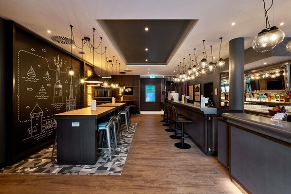 A modern bar area with a long counter, multiple stools, and a decorative wall with maritime illustrations.